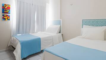 Habitación de hotel con dos camas, una ventana con cortinas y una pared con obras de arte coloridas.