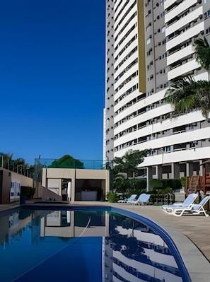 A high-rise hotel with a swimming pool and lounge chairs. - 4let Verano Ponta Negra (Natal)