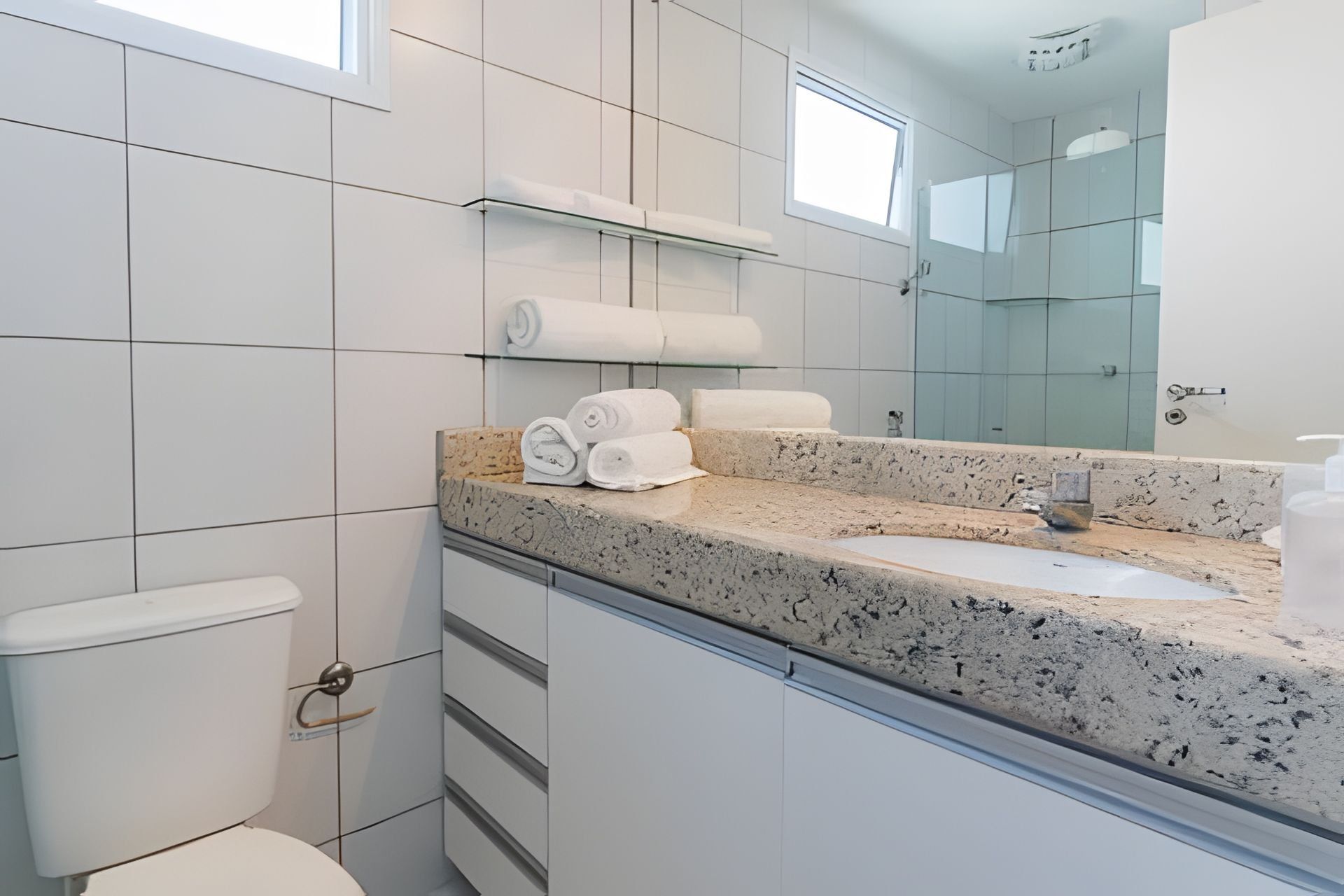 A modern bathroom with a granite countertop, a toilet, a glass shower enclosure, and a mirror.