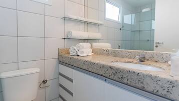 A modern bathroom with a granite countertop, a toilet, a glass shower enclosure, and a mirror.
