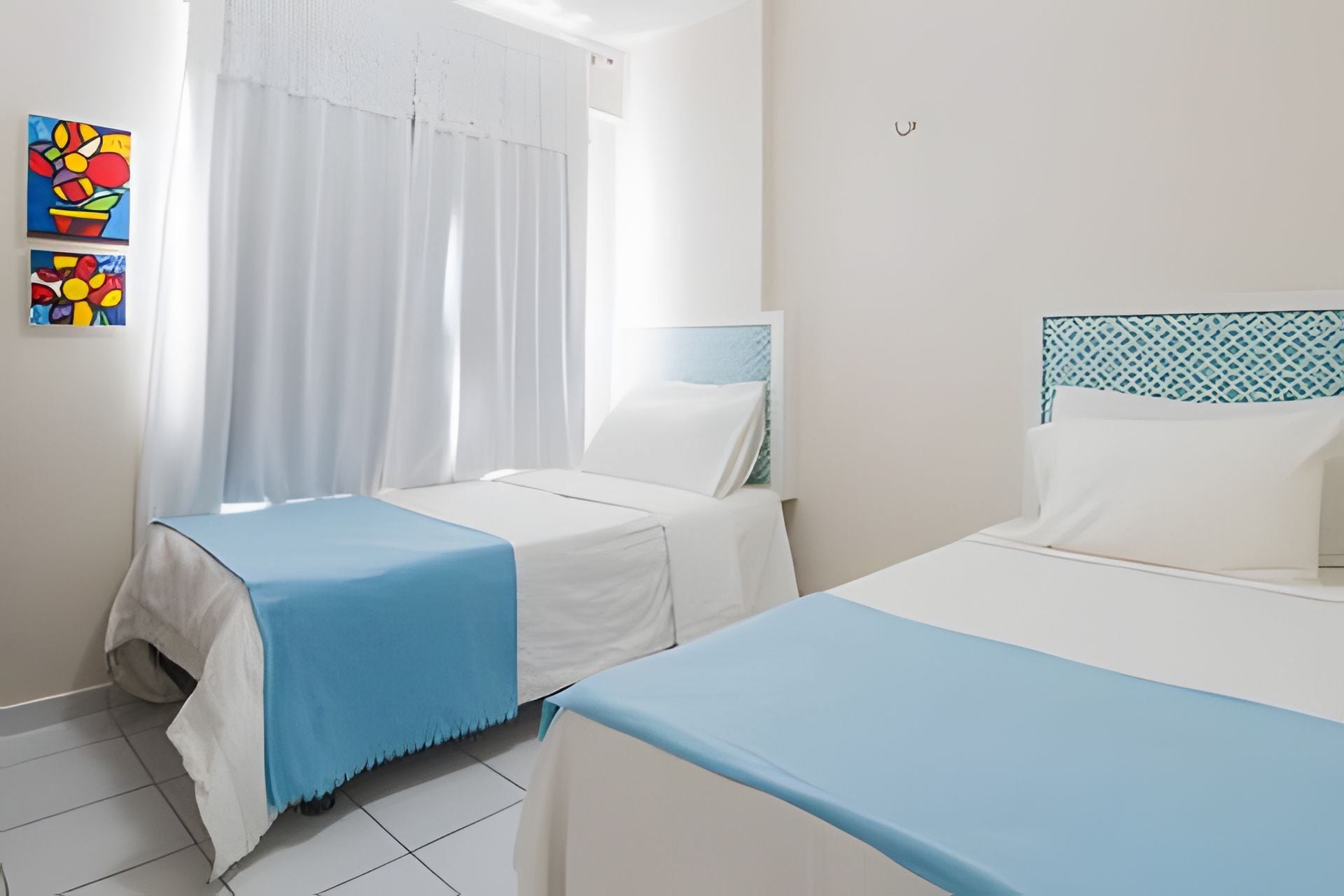 Habitación de hotel con dos camas, una ventana con cortinas y una pared con obras de arte coloridas.
