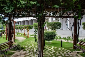 A covered outdoor area with a stone pathway, benches, and greenery. - 4let Verano Ponta Negra (Natal)