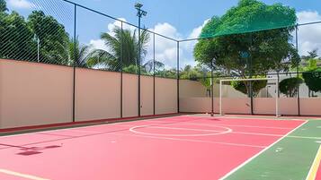 An outdoor basketball court with a net, surrounded by a fence and trees.