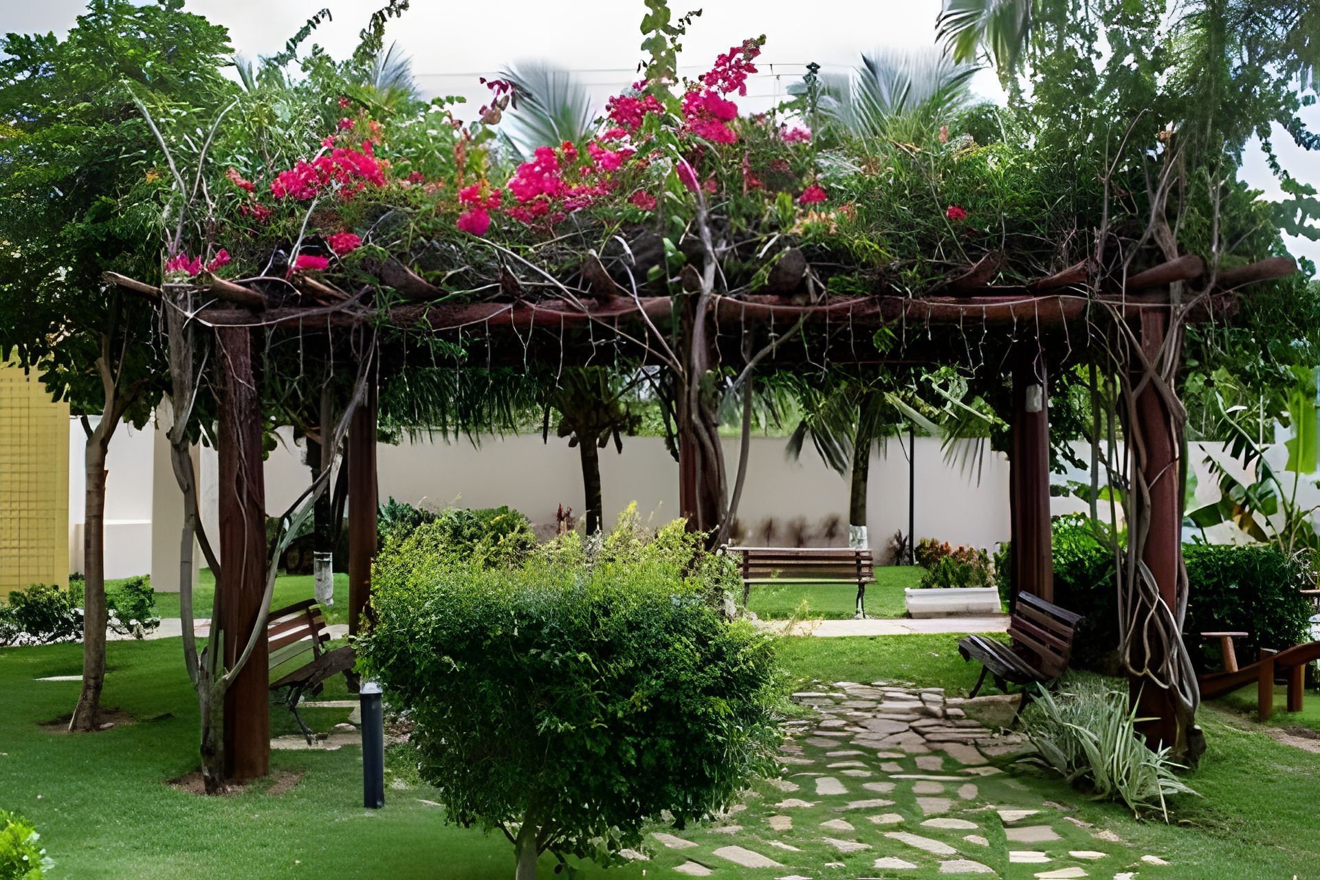 Um jardim com pérgula, bancos e um caminho de pedra.
