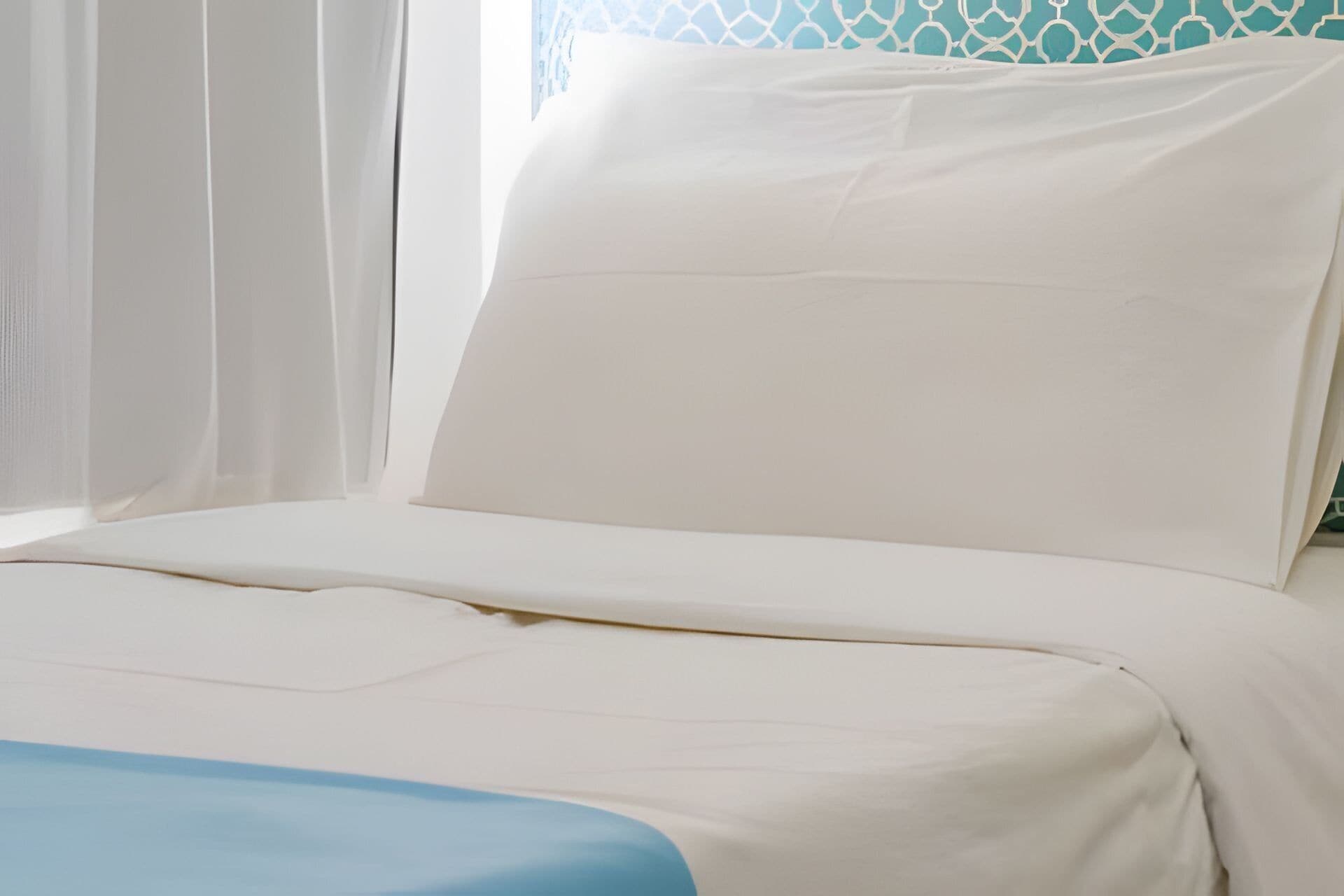 Cama com roupa de cama branca e detalhes em azul.