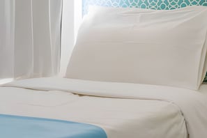 Un lit avec une literie blanche et un élément décoratif bleu.