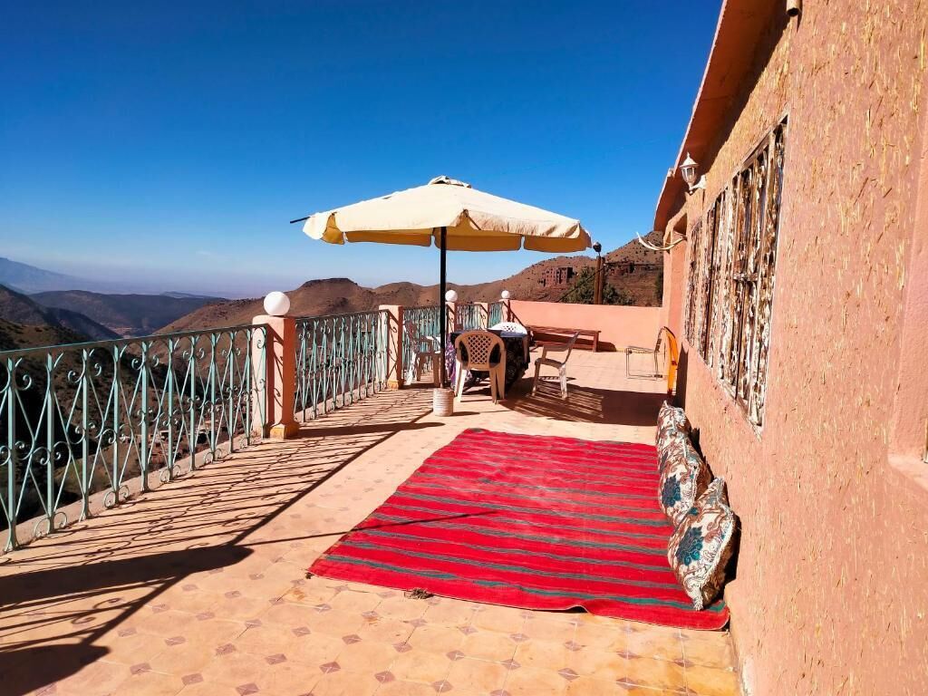 A balcony with a red mat, a table, chairs, and a white umbrella.