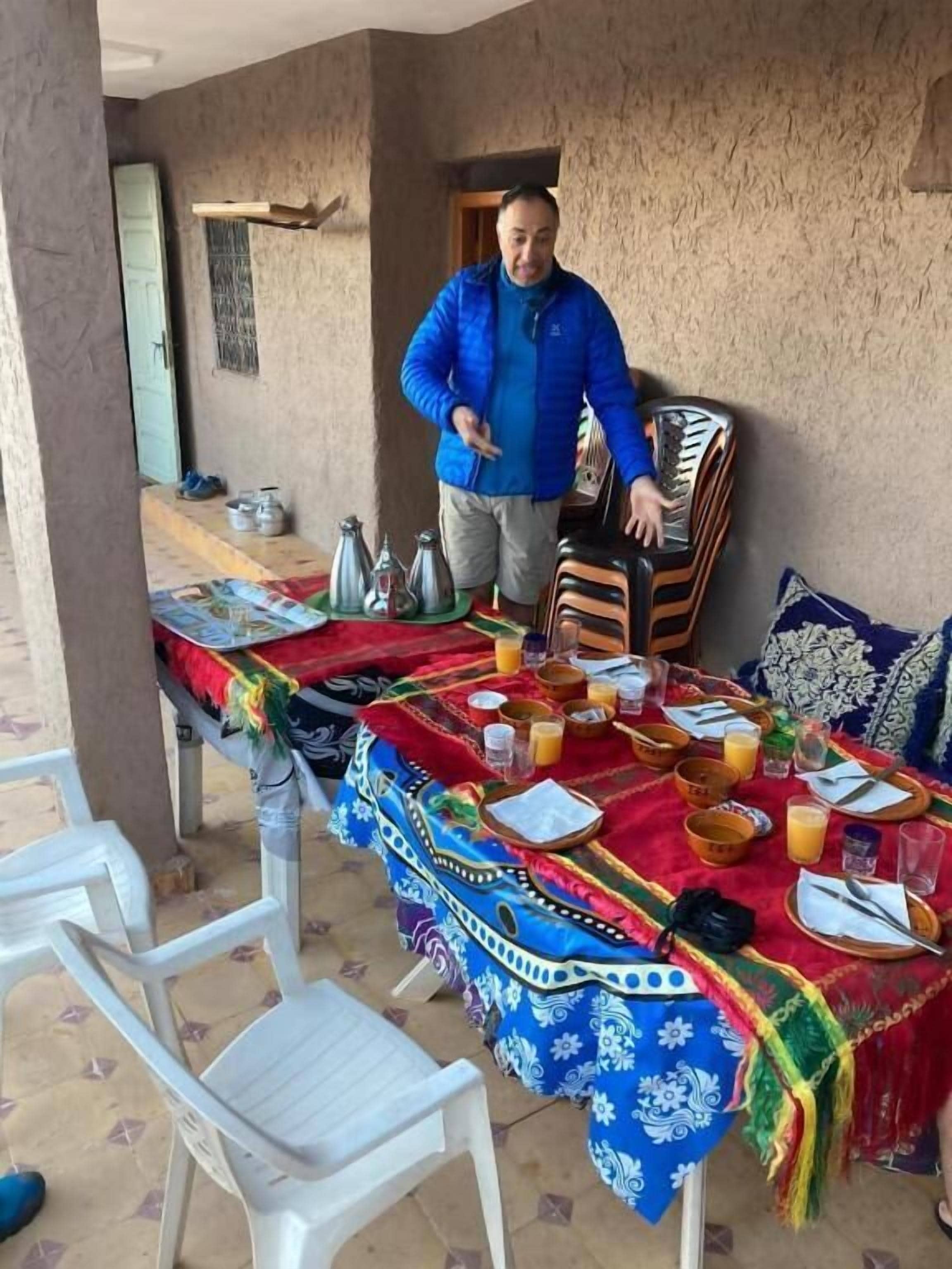 Una mesa de comedor dispuesta con platos, tazones y vasos, un hombre de pie junto a la mesa y una silla.