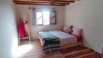 Une pièce avec un lit, une fenêtre avec des rideaux, un plafond en bois et un tapis à rayures.