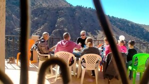 A group of people seated at an outdoor table with a mountainous backdrop.