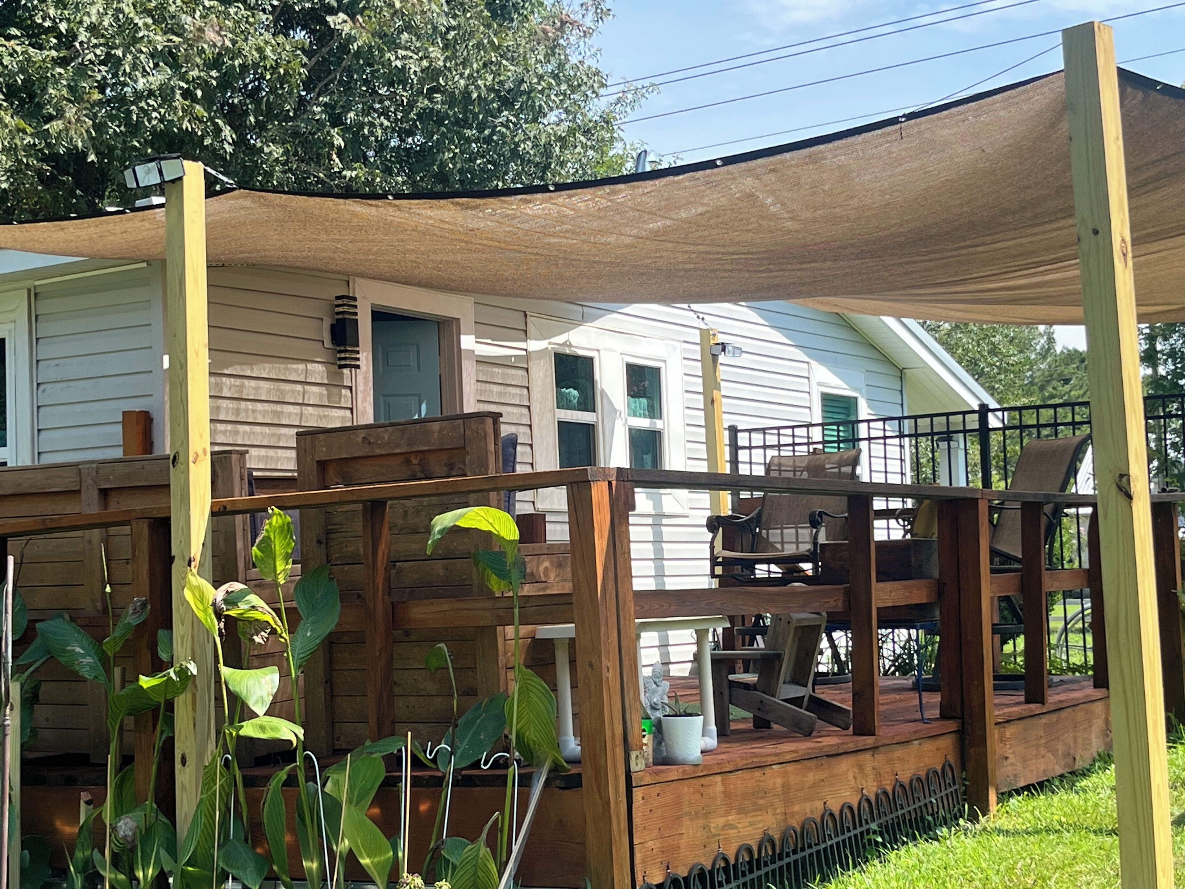 A wooden deck with a pergola, a white house with a porch, and a grassy yard.