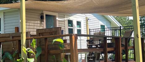 A wooden deck with a pergola, a white house with a porch, and a grassy yard.