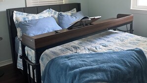 Une chambre à coucher avec un lit, une table de chevet, une fenêtre avec des stores et deux tableaux encadrés accrochés au mur.