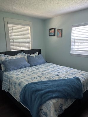 Un dormitorio con una cama, dos ventanas con persianas y dos cuadros en la pared.