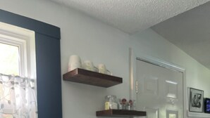 Une cuisine équipée d’une machine à café, une fenêtre avec des rideaux légers et une porte ornée d’un cadre de photo.