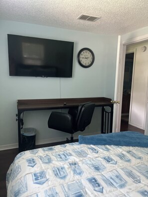 Ein Schlafzimmer mit einem Bett, einem Schreibtisch mit Stuhl, einem Fernseher und einer Wanduhr.