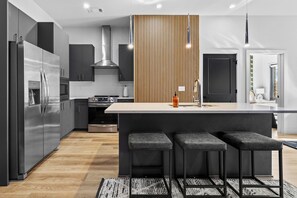 Una cucina moderna con elettrodomestici in acciaio inossidabile, una parete d'accento in legno e un'area bar con sgabelli.