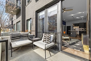 An outdoor seating area with a sofa and chairs, a glass door entrance to a kitchen, and a view of the street. - NEW! Chic Designer 2BR w/ Pool / Midtown Townhome (Nashville)