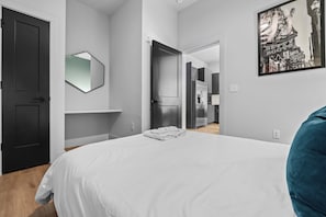 A modern bedroom with a large bed, a mirror, and a hallway leading to a kitchen. - NEW! Chic Designer 2BR w/ Pool / Midtown Townhome (Nashville)
