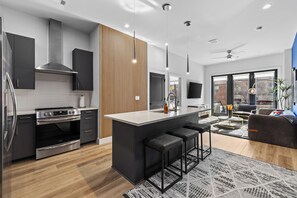 A modern kitchen with a central island, stainless steel appliances, and a wooden accent wall. - NEW! Chic Designer 2BR w/ Pool / Midtown Townhome (Nashville)