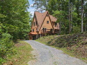 A two-story wooden house with a gravel driveway leading to a wooden deck. - Gingerbread House | Hot Tub, Fire Pit, Arcade Table (Gatlinburg)