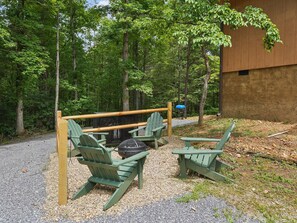 A forested area with a wooden deck, green Adirondack chairs, and a grill. - Gingerbread House | Hot Tub, Fire Pit, Arcade Table (Gatlinburg)