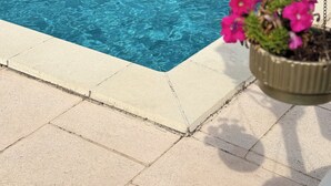 Una piscina con agua azul cristalina, rodeada por una terraza con baldosas.