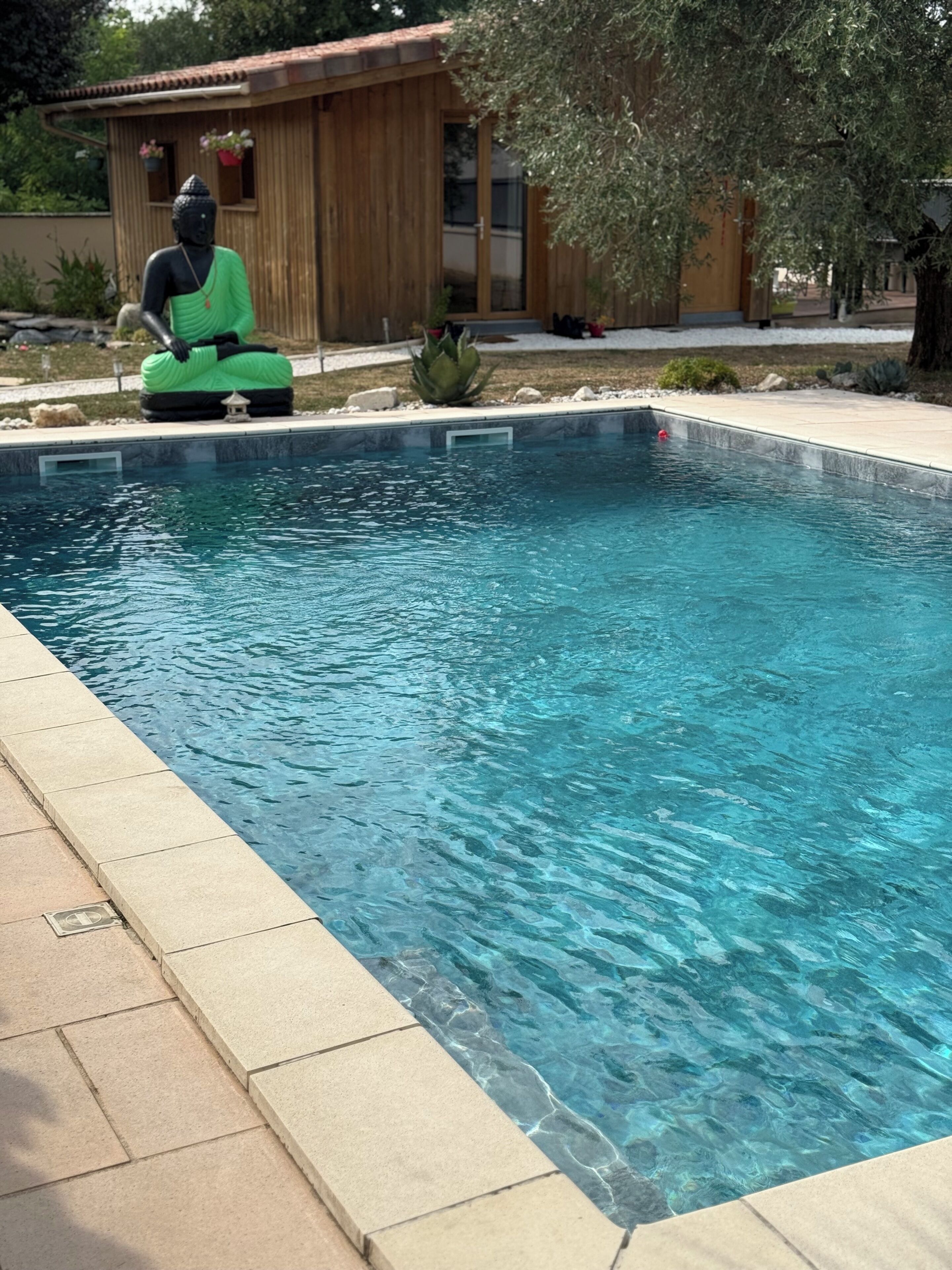 A swimming pool with a Buddha statue, surrounded by a wooden structure and greenery.