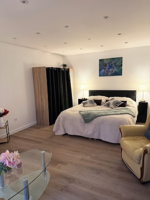 A bedroom with a bed, bedside lamps, a chair, a glass table with flowers, and a painting on the wall.