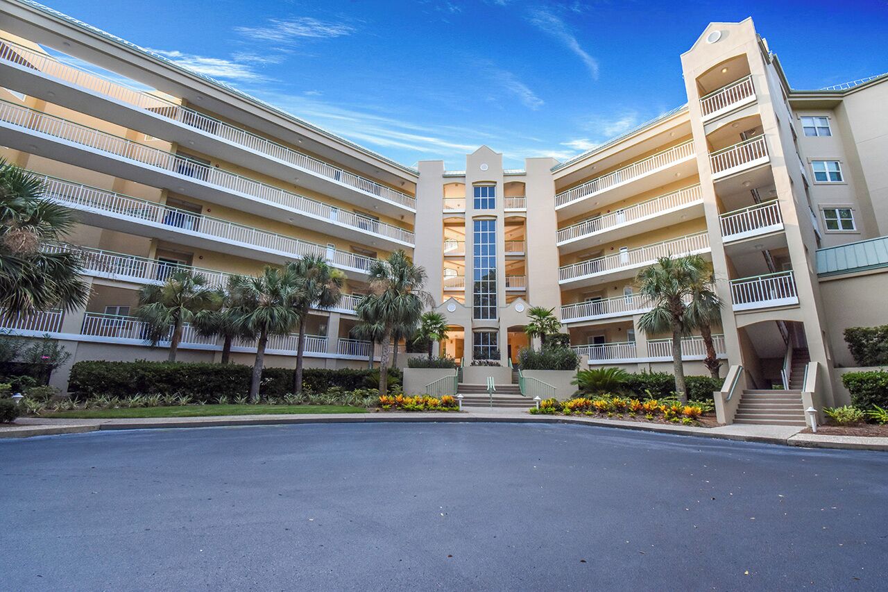 A multi-story hotel with a central entrance, balconies on each floor, and palm trees in the landscaping.