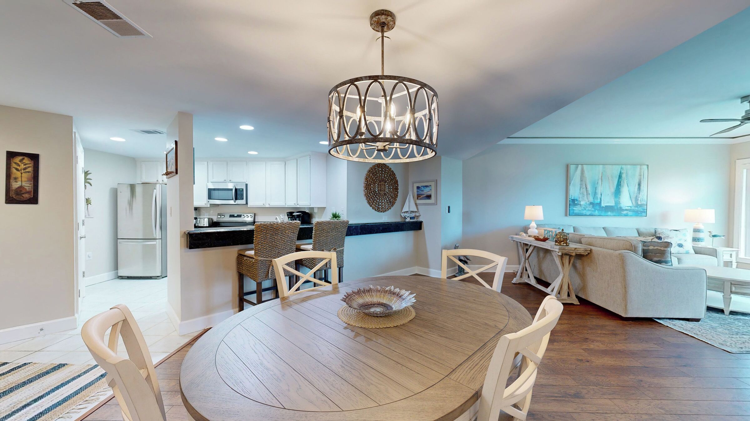 Une cuisine moderne avec des meubles blancs, un coin repas avec une table et des chaises en bois, et un salon avec un canapé et un tableau.