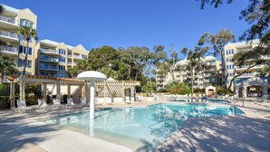 Ett hotellområde med en pool, solstolar, en pergola och ett kristallklart, blått poolvatten.