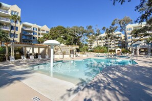 Ein Hotelpoolbereich mit Liegestühlen, einer Pergola und einem klaren, blauen Pool.