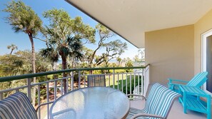 Ein Balkon mit Glastisch und Stühlen, der auf eine angelegte Grünfläche mit Bäumen und Meerblick blickt.