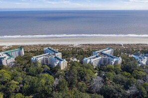 A coastal hotel with multiple buildings, surrounded by dense greenery and a beach in the background. - Oceanfront Coastal One Bedroom Corner Villa! (Hilton Head)