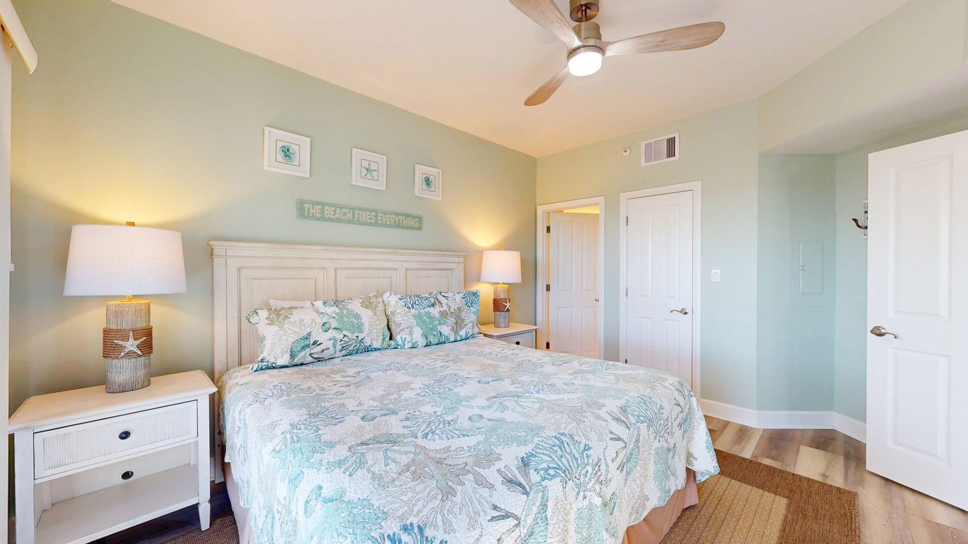 Une chambre à coucher avec un lit, deux tables de chevet avec des lampes, un ventilateur de plafond et un mur orné de tableaux.