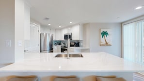 A modern kitchen with a central island, stainless steel appliances, and a large window. - Oceanfront Coastal One Bedroom Corner Villa! (Hilton Head)