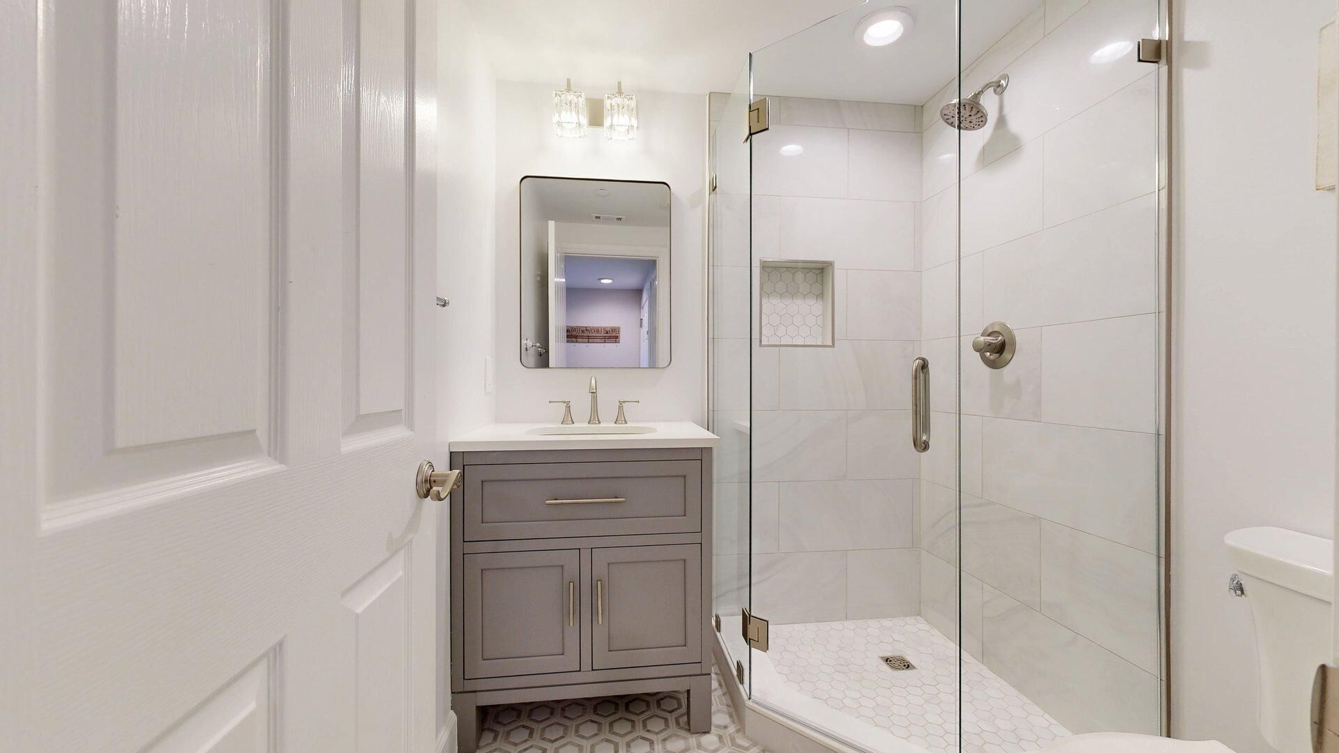 Un baño moderno con ducha de vidrio, tocador con espejo e inodoro.