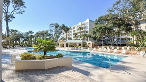 Un espace piscine d’hôtel avec des chaises longues et un bâtiment doté de nombreux balcons.