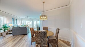 A spacious living room with a grey sofa, a dining table with woven chairs, and a hanging light fixture. - Oceanfront Coastal One Bedroom Corner Villa! (Hilton Head)