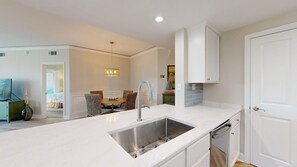Een moderne keuken met een roestvrijstalen spoelbak, witte kasten en een eethoek met rieten stoelen.