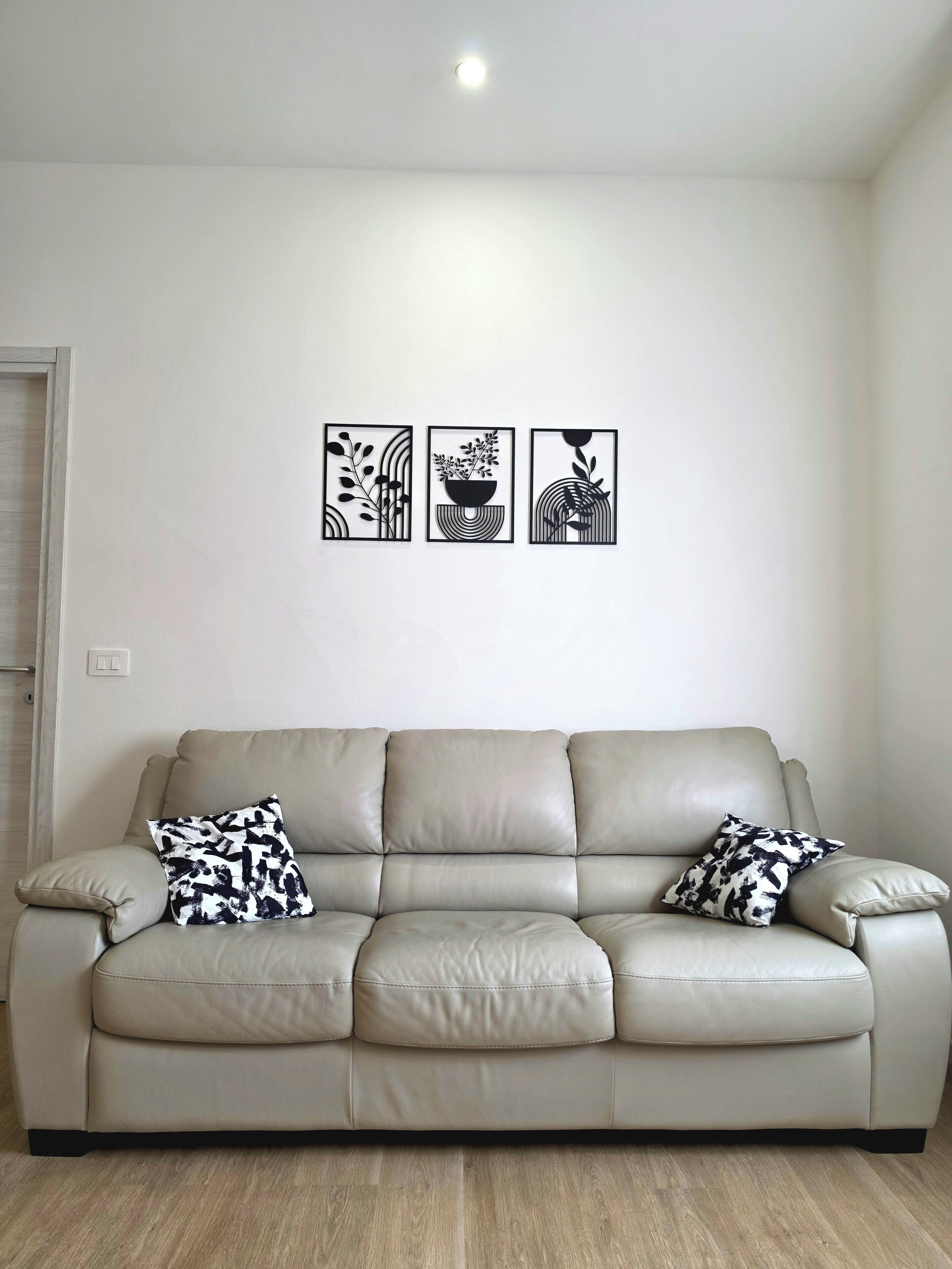 Ein sofasitz in neutraler Farbe aus Leder, mit zwei dekorativen Kissen mit Muster, einer Wandleuchte und drei gerahmten abstrakten Kunstwerken.