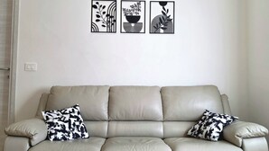 Un canapé en cuir aux tons neutres, agrémenté de deux coussins décoratifs à motifs, d’un luminaire fixé au mur et de trois œuvres d’art abstraites encadrées.