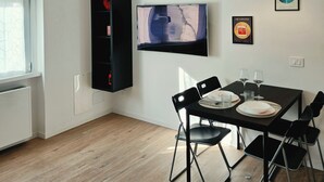 Un espace repas moderne avec un téléviseur à écran plat fixé au mur, une table à manger avec des chaises et un luminaire suspendu.