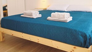 Une chambre avec un cadre de lit en bois, une couvre-lit bleue, deux serviettes blanches soigneusement pliées, une armoire blanche et trois œuvres d’art décoratives aux messages inspirants accrochées au mur.