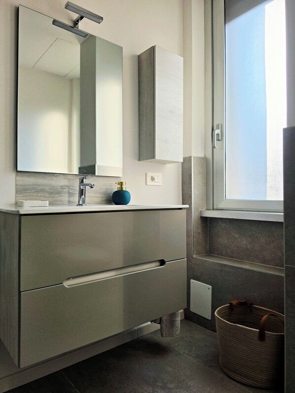 A bathroom with a large mirror, a modern faucet, a blue soap dispenser, and a wicker basket.