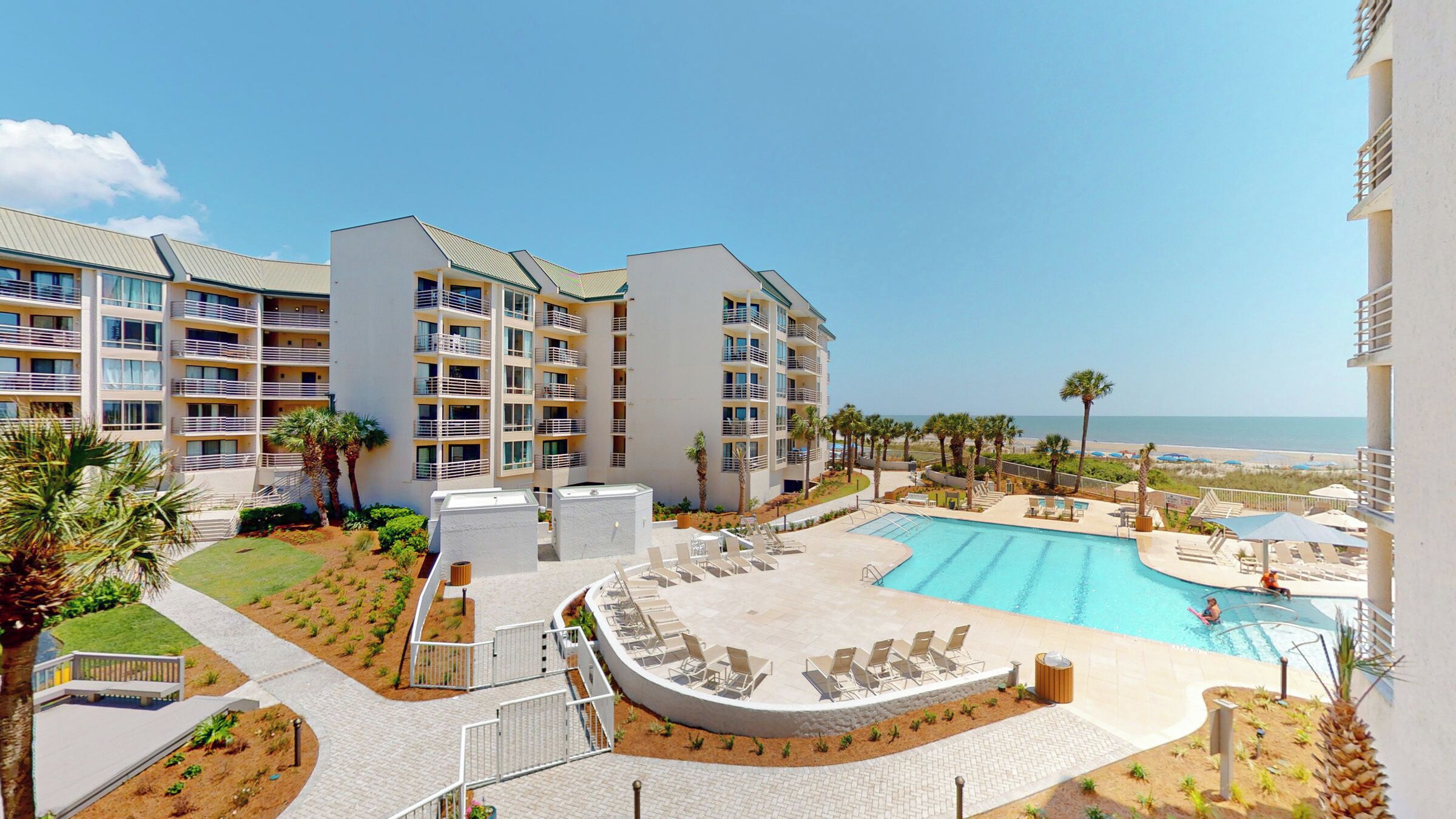 A hotel with multiple floors, a swimming pool, and a view of the beach.