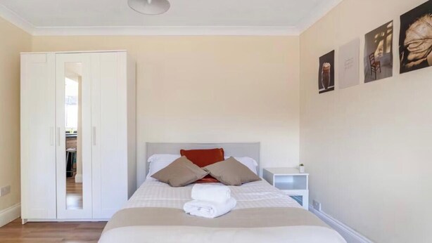 A hotel room with a bed, a wardrobe, a nightstand, and a wall with framed pictures.