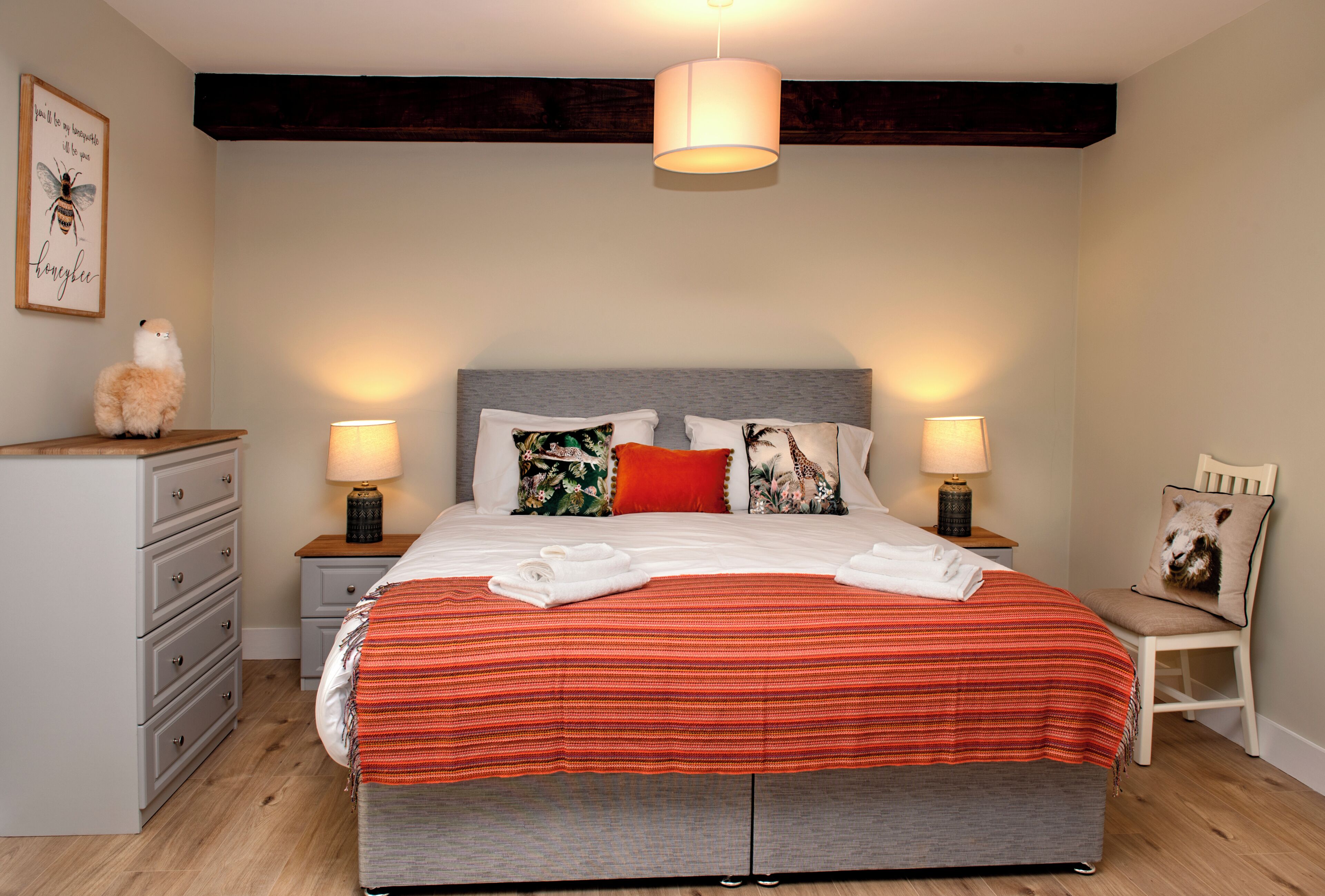 A bedroom with a large bed, two bedside tables with lamps, a dresser, and a chair.