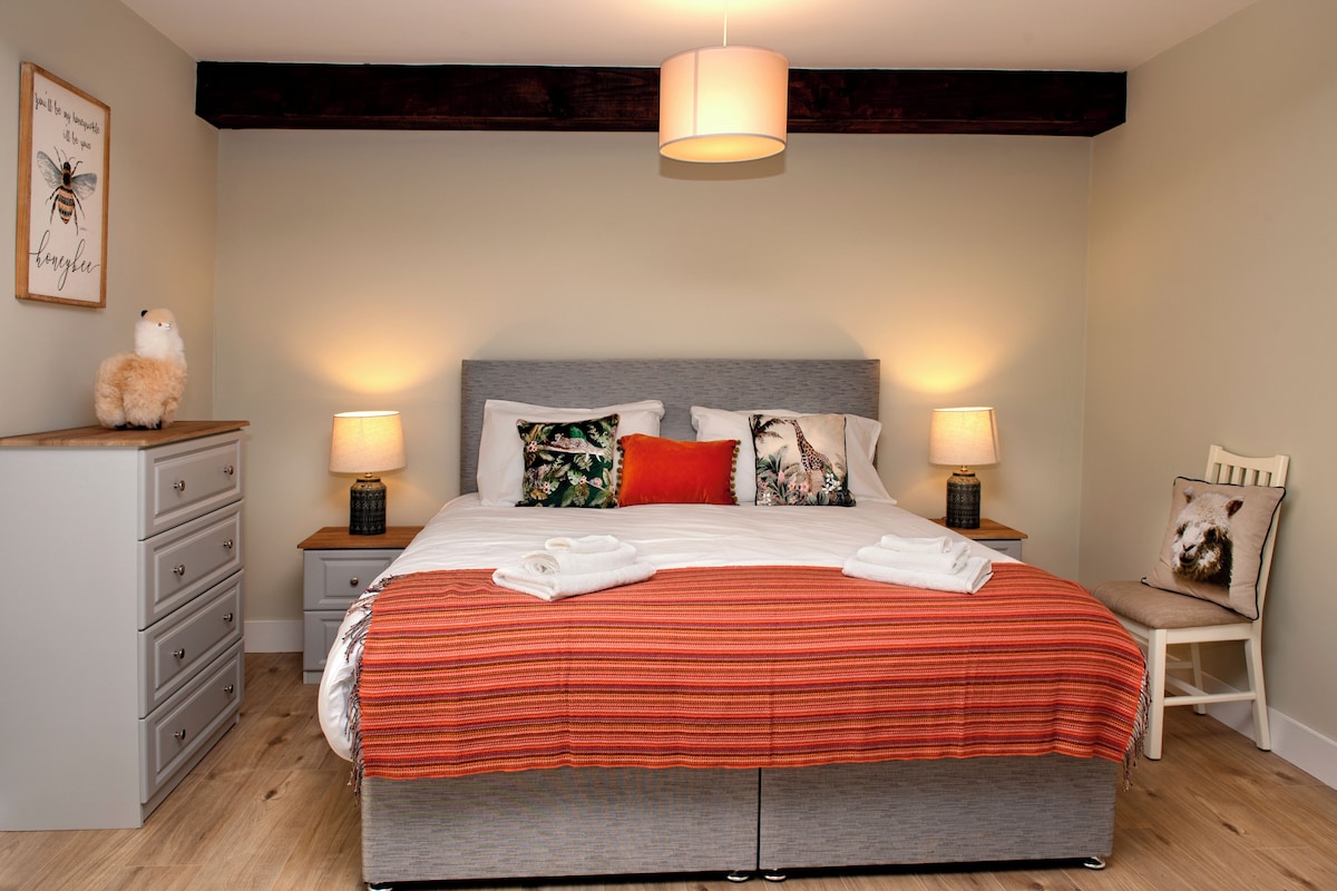 A bedroom with a large bed, two bedside tables with lamps, a dresser, and a chair.